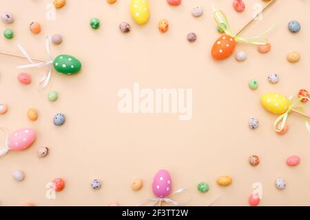 Bunte Ostereier auf Stöcken und Schokoladen-Mini-Bonbons auf beigefarbenem Hintergrund, Draufsicht Stockfoto