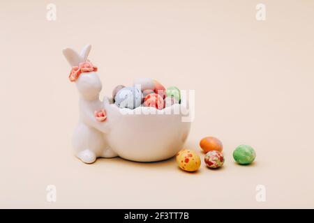 Osterschokolade Mini Bonbons im Keramikständer mit Hase Figur auf beigem Hintergrund Stockfoto