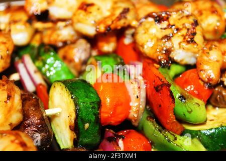 Nahaufnahme von gegrillten Gemüsespiessen mit gegrillten Garnelen-Spiessen außerhalb des Fokus oben im Bild. Stockfoto