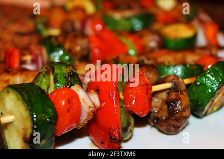 Nahaufnahme von gegrillten Gemüsespießen und gegrillten Garnelenspießen in wechselnden Reihen auf einem weißen Serviergericht. Stockfoto