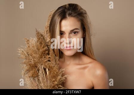 Schöne junge weibliche Modell mit lockeren Haaren hält trockene Pampas Gras in ihren Händen. Das Konzept der Naturkosmetik aus Weizenkörnern. Hautpflege. Stockfoto