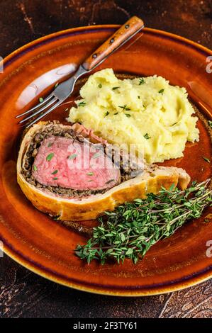 Beef Wellington Gebäck mit Kartoffelbrei auf einem rustikalen Teller. Dunkler Hintergrund. Draufsicht Stockfoto