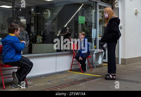 Carmarthenshire, Großbritannien. März 2021, 17th. Eine Frau mit Kindern wartet vor einem Friseursalon in Wales, Großbritannien.Acht weitere Menschen sind in Wales an Coronaviren gestorben und die Infektionsrate ist insgesamt leicht angestiegen. Kredit: SOPA Images Limited/Alamy Live Nachrichten Stockfoto