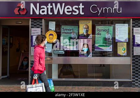 Carmarthenshire, Großbritannien. März 2021, 17th. Eine Frau, die eine Maske trägt, während sie Einkaufstaschen trägt, geht an einer NatWest-Bank in Wales vorbei.Acht weitere Menschen sind in Wales an einem Coronavirus gestorben und die Gesamtinfektionsrate ist leicht gestiegen. Kredit: SOPA Images Limited/Alamy Live Nachrichten Stockfoto