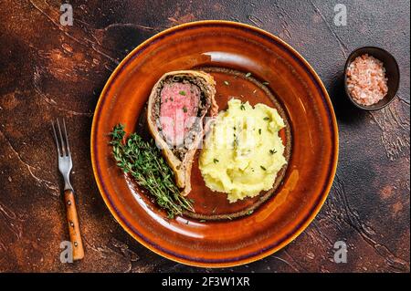 Beef Wellington Gebäck mit Kartoffelbrei auf einem rustikalen Teller. Dunkler Hintergrund. Draufsicht Stockfoto