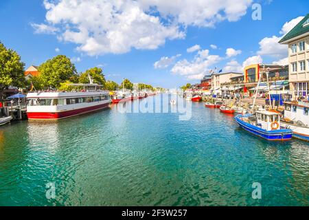 Geschäfte, Boote und Cafés am Alten Strom Canal in der Nähe der Hafen im Zentrum von Warnemünde, in der Nähe von Rostock an der Küste im Norden von Deutschland. Stockfoto