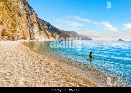 Eine Frau wagt im türkisblauen grünen Meer vor dem abgeschiedenen Paradies, oder Chomi Beach auf der Insel Korfu, Griechenland. Stockfoto