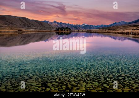 Transparant kristallklares Wasser zeigt die Felsen auf dem Boden Des Sees mit Bergreflexionen bei Sonnenuntergang Stockfoto