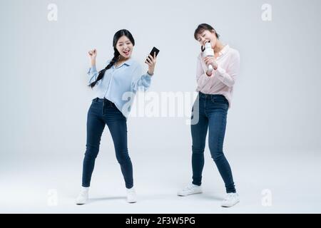 Zwei asiatische Frauen, Schwestern singen mit kabellosem Mikrofon und mobile Karaoke-Anwendung am Telefon Stockfoto