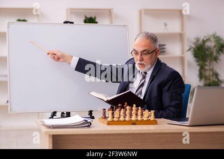 Alter Geschäftsmann Angestellter, der Schach am Arbeitsplatz spielt Stockfoto