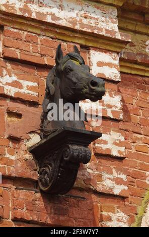 Skulptur des Pferdekopfes auf der Ziegelmauer eines verlassenen Gestüts aus dem 19th. Jahrhundert (Pskow Oblast, Russland) Stockfoto