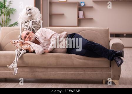 Alter Mann sitzt auf dem Sofa mit dem weiblichen Skelett In unsterbst Liebe Konzept Stockfoto