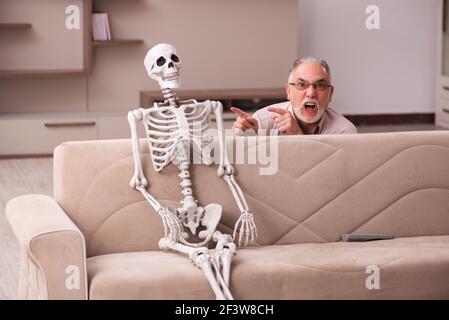 Alter Mann sitzt auf dem Sofa mit dem weiblichen Skelett In unsterbst Liebe Konzept Stockfoto