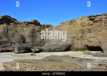 Erodierende felsige Formation mit senkrechter Wand und kleinen Höhlen, die bei Ebbe am Sandstrand freigelegt sind. Stockfoto