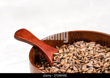 Segenmilchdistel Samen - Silybum marianum - in kleinen Holzbecher mit Löffel auf weißem Stein wie Brett, Nahaufnahme Detail Stockfoto