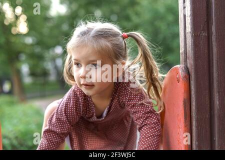 Kleines Mädchen in roten Kleid spielt auf dem Spielplatz an einem Sommertag. Gesunde Sommeraktivitäten für Kinder. Stockfoto