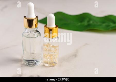 Set aus einer Glas-Kosmetikflasche mit einem Tropf auf einem Marmorboden mit Blättern. Naturkosmetik-Konzept, natürliches ätherisches Öl mit 24K Gold inkl Stockfoto