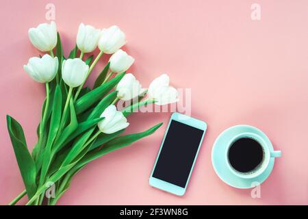 Tasse Kaffee, Smartphone und weiße Tulpen auf rosa Hintergrund, Draufsicht. Frauentag oder Muttertag Konzept. Flach liegend, Kopierplatz. Stockfoto