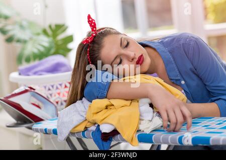 Erschöpfte schöne junge Frau, die sich auf das Bügelbrett lehnte Stockfoto