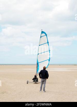 Sand Yacht Land Segeln am Strand Plage de Ouistreham in Frankreich. Ein Mann, der auf eine sandige Yacht schaut. Stockfoto