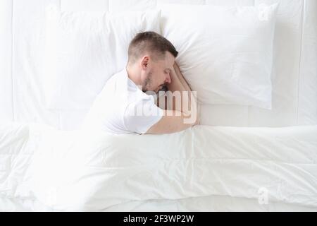 Der junge Mann schläft friedlich auf dem großen weißen Bett Stockfoto