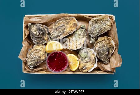 Schachtel mit geöffneten frischen Austern, Zitrone und Essig Zwiebelsouce auf blauem Hintergrund, Draufsicht Stockfoto