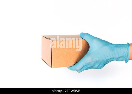 Kontaktlose Lieferung, Online-Shopping-Konzept. Hand in medizinischen Handschuh gibt Handwerk Box auf blauem Hintergrund. Banner, Kopierbereich. Sichere Verpackung während Stockfoto