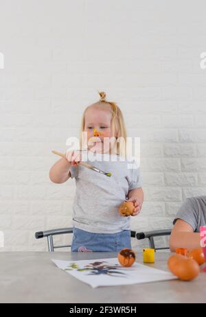 Ein kleines Mädchen in Farbe geschmiert lernt Eier zu malen Für die Osterferien Stockfoto