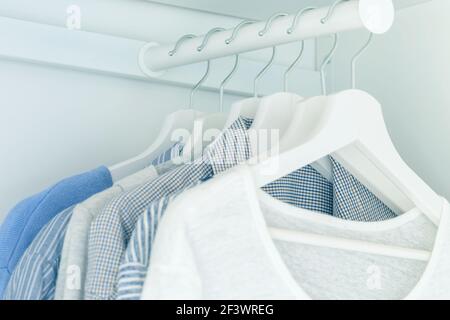 Weißer Kleiderschrank mit hellblauen Hemden und Blusen, die an Kleiderbügeln hängen. Stockfoto