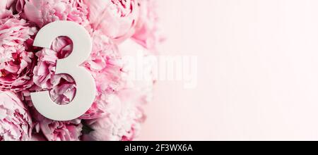 Kreatives Layout. Rosa Pfingstrosen Blüten und Ziffer drei 3. Geburtstagskarte. Jubiläumskonzept. Draufsicht. Speicherplatz kopieren. Stilvolles weißes Ziffernzeichen Stockfoto
