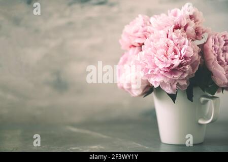 Rosa Pfingstrosen Blumen in weißem Becher auf Marmor Vintage Hintergrund. Hochzeit, Geburtstag, Blumenstrauß zum Jahrestag. Speicherplatz kopieren. Trendige, pastellfarbene Blumenkomposition Stockfoto