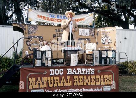 Ein Reisender Outdoor-Showman und Entertainer, Doktor Barth und seine ‘Medicine Show’, Florida, USA im Jahr 1990. Der Doc fördert seine Naturheilmittel, Tränke und Elixiere. Er ist auch Bauchredner, mit dem Dummy seines Bauchredner links. Ein Schild auf der Rückseite sagt: ‘schmerzlose Zahnextraktion $1,00’. Dies ist eine ungewöhnliche Besetzung und der Schwerpunkt hier scheint auf der Unterhaltung zu sein. Im wirklichen Leben würden viele einen Medizin-Show-Arzt als ‘Quack’ oder Fälschung ansehen. Dieses Bild stammt aus einer alten amerikanischen Amateur-Farbtransparenz – einem Vintage-Foto aus dem Jahr 1990s. Stockfoto