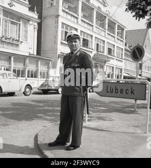 1960s, historisches Foto von J Allan Cash eines uniformierten deutschen Polizisten, mit Hut und Knüppel, der an der Straßenecke bei Lübeck, der zweitgrößten Stadt des Landes Schleswig-Holstein, stand. Stockfoto