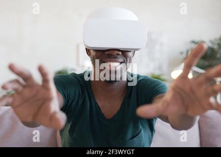 Afrikanisch glücklich Mann in vr Brille spielen Videospiel und Gestikulieren auf dem Sofa Stockfoto