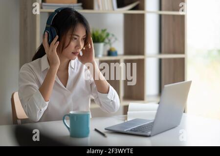 Schöne asiatische Frau in Kopfhörern haben Videoanruf entfernten Klasse mit Lehrer mit Laptop - Online-Lernkonzept. Stockfoto