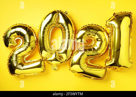 Goldene Folienballons machten Zahlen 2021 auf gelbem Hintergrund mit hellen Bokehs. Banner, Kopierbereich. Frohes neues Jahr Feier Partei. Grüße und Stockfoto