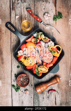 Roher, ungekochter Lachsfisch mit Gemüse, Kräutern, Gewürzen in einer eisernen Bratpfanne auf Holzboden. Draufsicht, Kopierbereich. Gesunde Ernährung. Abendessen Stockfoto