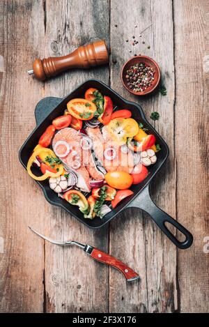 Roher, ungekochter Lachsfisch mit Gemüse, Kräutern, Gewürzen in einer eisernen Bratpfanne auf Holzboden. Draufsicht, Kopierbereich. Gesunde Ernährung. Abendessen Stockfoto