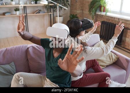 Junge aufgeregt Paar in Gläsern sitzen auf Sofa zurück zu Zurück und spielen Videospiel zu Hause Stockfoto