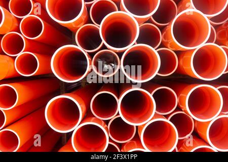 Ein Stapel von orangefarbenen elektrischen PVC-Kabelrohren in Reihen in einem Lagerhaus, das ein wiederholtes Muster von Kreisen gibt. Stockfoto