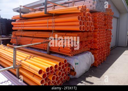 Stapel von orangefarbenen, gelben und weißen PVC-Elektrorohrleitungen in einem Lagergebäude. Stockfoto