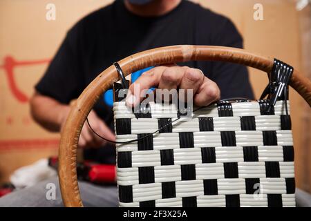Villemer (Paris area), September 2020 : Maison Gatti’s workshop, rattan furniture maker. Close-up shot of the hands of a worker weaving a chair. Plast Stockfoto