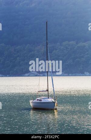 Segelyacht auf einem schönen See inmitten bewaldeter Berge Stockfoto