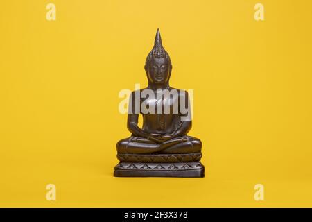 Ruhige kleine Bronze Thai buddha Statue gegen eine gelbe nahtlose Hintergrund in meditativer Haltung Stockfoto