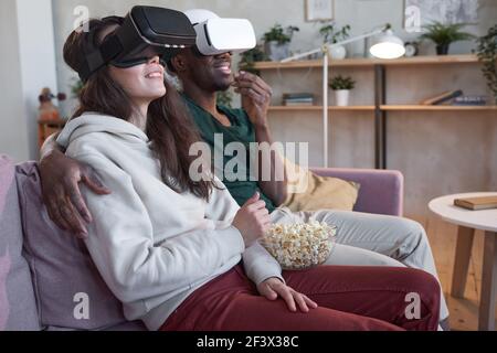 Junges Paar in vr Brille genießen von Film zusammen zu sehen Mit Popcorn zu Hause Stockfoto