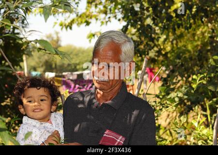 Portraitfoto eines indischen älteren glücklichen Großeltern und kleine Enkelkinder stehen im Garten mit einem Lächeln, Indien Stockfoto