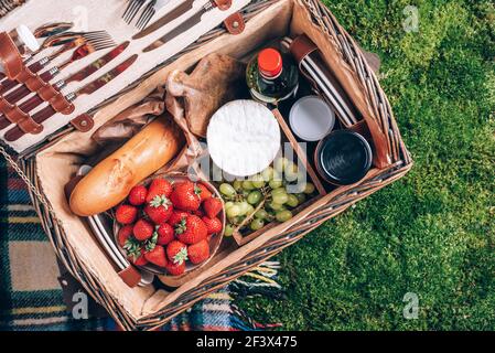 Toller Picknickkorb mit Käse, Erdbeeren, Trauben, Baguette, Wein zum Picknick auf karierten grünen Hintergrund. Draufsicht. Speicherplatz kopieren. Sommerfamilie Stockfoto