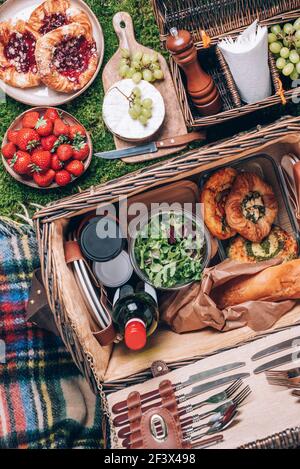 Großer Picknickkorb mit Käse, Erdbeeren, Trauben, Baguette, Pizza, Salat, Wein zum Picknick auf karierten grünen Hintergrund. Draufsicht. Speicherplatz kopieren Stockfoto