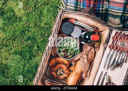 Picknick-Set mit Obst, Käse, Honig, Erdbeeren, Trauben, Baguette, Wein, Pizza, Salat, Weidenkorb für Picknick auf karierten, grünen Gräsern. Draufsicht Stockfoto