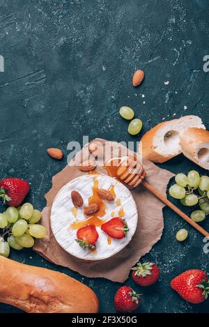 Französischer Camembert-Käse, serviert auf Trauben, Honig, Mandeln, Erdbeeren und Baguette auf dunklem Grund. Draufsicht. Speicherplatz kopieren. Romantische Dattsnacht Stockfoto